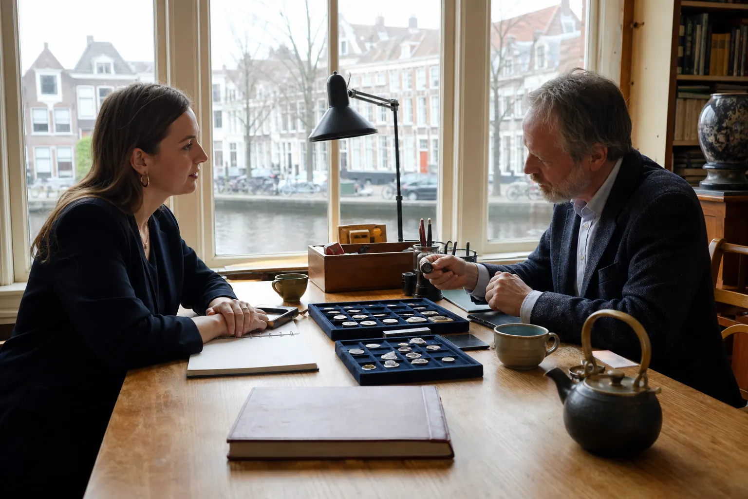 Consultgesprek over Griekse munten aan een tafel in het Leidse Rapenburg-atelier met grachtlicht